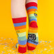 Back view of rainbow-striped socks, showing the colourful bands and a peek of the sock label, “Katie Abey Socctopus,” with confetti surrounding the feet.