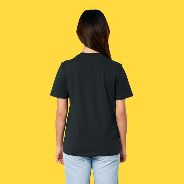 Model wearing the black Cute But Feral Cat adults t shirt shown from the back. Organic cotton unisex tee with a loose drape and casual fit, styled with jeans on a bright yellow background.