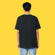 Model wearing the black Cute But Feral Cat adults t shirt shown from the back. Relaxed unisex fit with short sleeves and crew neck, styled with light blue jeans against a yellow background.