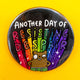 A round badge on a bright yellow background featuring the phrase "Another Day of Resisting Despair" in bold white and rainbow lettering. A brown cartoon bear character stands proudly at the bottom, with rainbow rays and sparkles behind them.