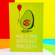 Here is your birthday avocardo A6 greeting card designed and printed in the UK by Katie Abey. The green base front cover features an avocado with arms, legs and a smiling face holding a balloon. The underneath text reads 'here is your birthday avocardo' with the card being underlined as the pun. The card is stood up 