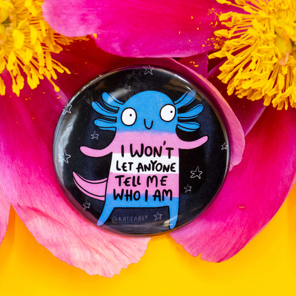 Katie Abey badge nestled in bright pink and yellow flower petals. It features a blue and pink axolotl character with the empowering phrase: “I won’t let anyone tell me who I am,” set against a starry black background.