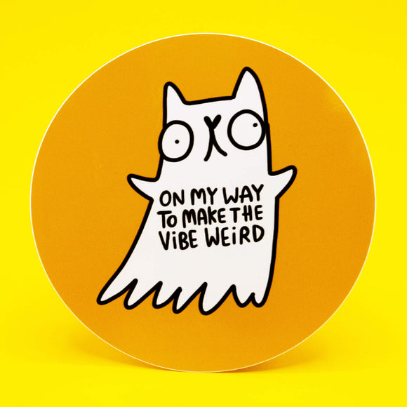 A round vinyl sticker featuring a quirky white ghost cat illustration by Katie Abey on an orange background. The ghost cat has wide eyes and the text reads On My Way To Make The Vibe Weird. Premium vinyl sticker, 10 cm diameter, durable and wipe clean. Perfect for laptops, notebooks, water bottles, and gifts for people who love cute and weird art.