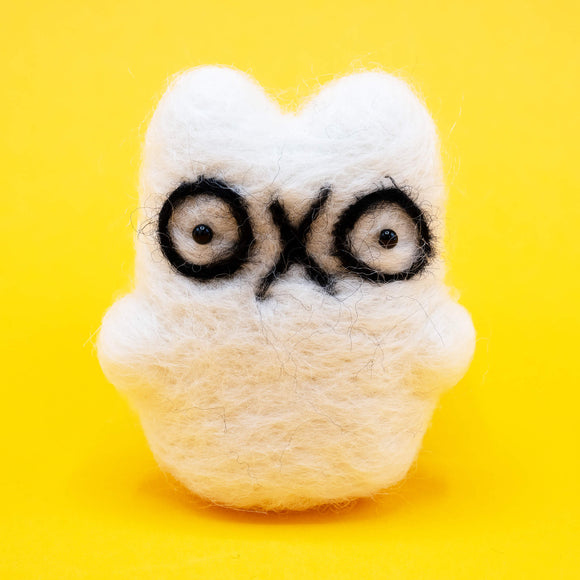 A handmade needle felted ghost cat by Katie Abey x Ghost Of The Month shown on a bright yellow background. The white wool ghost cat has big black outlined eyes and a cute quirky expression. Felted by hand, approx 8cm by 5cm, this decorative collectible is perfect for fans of weird cute art and handmade gifts.