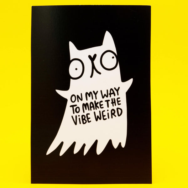 Black A6 postcard featuring a white ghost cat illustration by Katie Abey with wide eyes and a quirky expression. The ghost cat has the text On My Way To Make The Vibe Weird printed on its body. The postcard is displayed against a bright yellow background. Fun spooky design for fans of weird art and positive vibes.