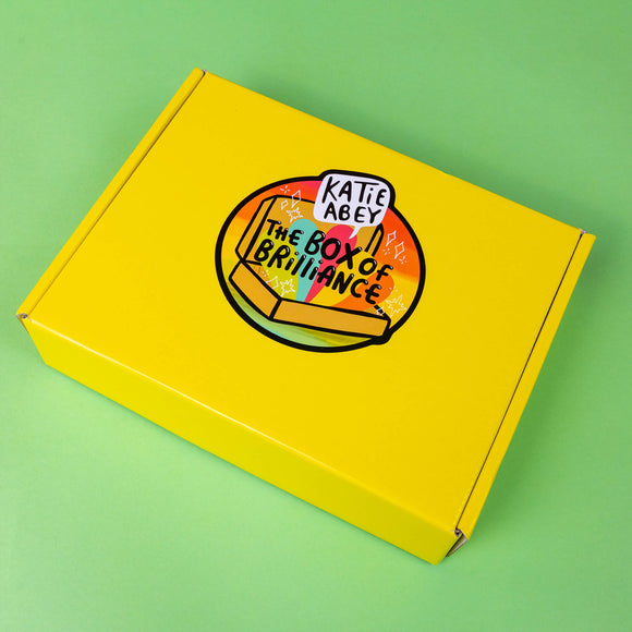The Box of Brilliance - Subscription Boxes - One Time Purchase on a green background. The yellow cardboard box has a rainbow katie abey box of brilliance logo in the middle.