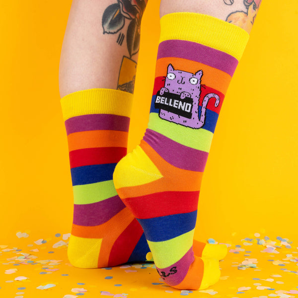 A playful angled pose of the socks, showing both the Bellend cat design and the bright stripes in full glory, with tattooed legs adding extra flair.