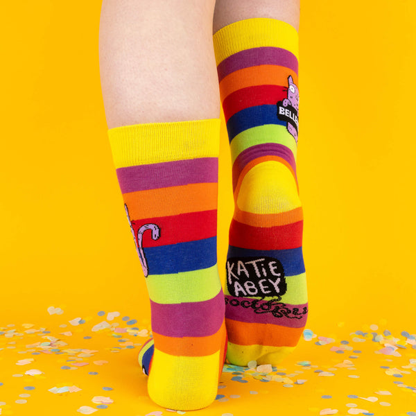 A rear view of the socks with “Katie Abey” branding on the soles, set against a yellow confetti-strewn floor, perfect for showing off every bold detail.