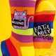 A close-up of the socks’ design featuring the purple cat with its sassy slogan, alongside “Katie Abey” branding on the soles, with vibrant rainbow stripes tying it all together.