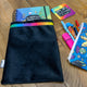 A black oracle bag with a rainbow ribbon around the top with the happy and enchanted planner popping out the top. it has a coaster and pencil case in the shot on a wooden table