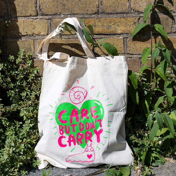 Snail Boi Tote bag. A white tote bag with pink text reading 'care but don't carry' on top of a green heart with pink snail illustrations.