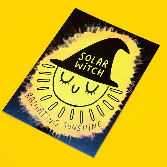 A bright A6 postcard by Katie Abey featuring a smiling sun wearing a black witch hat that says "Solar Witch", with the caption "Radiating Sunshine" underneath. The cheerful yellow and black design encourages positivity and weirdness. Printed on sturdy card with a smooth finish, perfect for gifting or displaying.