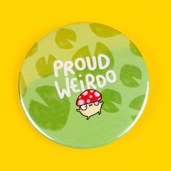 Circular badge by Katie Abey featuring the phrase "Proud Weirdo" in bold white text alongside a quirky red-spotted mushroom character with glasses. Set against a leafy green background, this fun and whimsical design celebrates individuality and embracing your unique weirdness. Ideal for adding personality to jackets, backpacks, or any accessory, this badge is a playful nod to being unapologetically yourself. Katie Abey’s illustration encourages you to stand out and be proud.