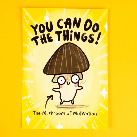 Katie Abey's motivational art print features "The Mushroom of Motivation," a cheerful mushroom character with a dark brown cap and quirky eyes, set against a vibrant yellow background. The bold text, "You Can Do The Things!" inspires positivity and determination, surrounded by sparkles for a fun, uplifting design. Perfect for adding a whimsical touch to any space, this print celebrates individuality and determination.