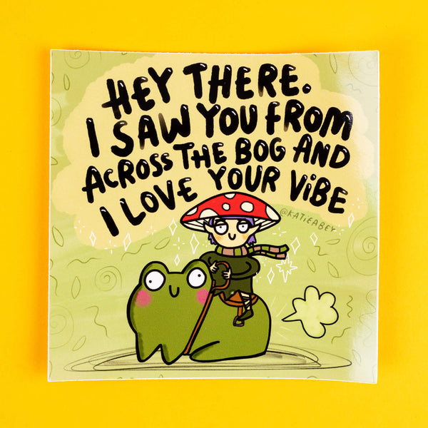 Whimsical square sticker by Katie Abey featuring a mushroom elf with a red-spotted cap riding a frog, captioned with "Hey there. I saw you from across the bog and I love your vibe." The vibrant green background is adorned with sparkles and swirls, exuding a playful and weirdly wonderful vibe. Perfect for adding personality to your belongings. Displayed on a bright yellow backdrop.