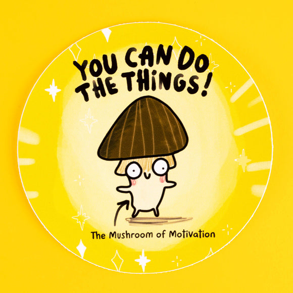 A motivational circular sticker featuring a cheerful illustrated mushroom with a dark brown cap, quirky eyes, and rosy cheeks, paired with the uplifting text "You Can Do The Things!" in bold black letters. Below, it reads "The Mushroom of Motivation." Designed by Katie Abey, this sticker combines humour and positivity to inspire. The yellow background is adorned with sparkles, radiating good vibes. Perfect for decorating laptops, notebooks, or anywhere needing a boost of encouragement.