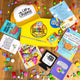 Contents of Box of Brilliance on wooden floor with rainbow pom poms scattered