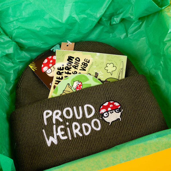 Katie Abey's "Proud Weirdo" gift set packed in green tissue paper, featuring a cosy green beanie with a mushroom embroidery and cheerful stickers, such as "I love your vibe." Ideal for weirdos who love colourful, quirky gifts that celebrate individuality.