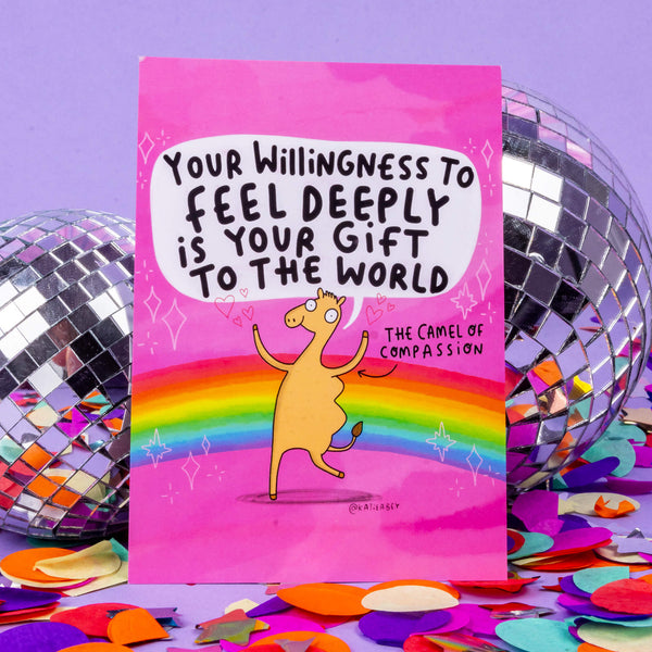 A pink and rainbow postcard with a dancing camel drawn by Katie Abey with the quote 'YOUR WILLINGNESS TO FEEL DEEPLY IS YOUR GIFT TO THE WORLD' it also has an arrow pointing at the camel with 'The Camel of Compassion'