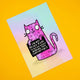 Angled view of Katie Abey’s “I’m Not Being Rude” Cat Art Print. The pink doodle-style cat holds a cheeky sign that reads, “I’m not being rude, I’m just not actively making you comfortable.” A vibrant A4 signed print with matte finish, ideal for quirky home décor and lovers of weird, playful art.