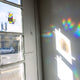 A see through rainbow making sun catching sticker that has a rainbow cat holding a sign saying keep on looking for those fucking rainbows casting a rainbow on a wall