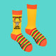 A flat-lay of Katie Abey's bright yellow socks with orange accents and rainbow-striped soles. Features a grey hamster with chainsaws under a sparkly rainbow, with "Woke Up and Chose Violence" text. Perfect for lovers of colourful, quirky accessories with a touch of chaos.