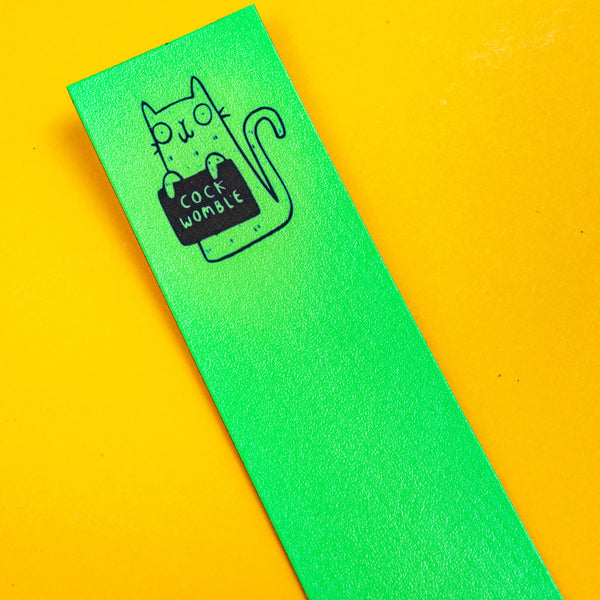 the top of a bright green leather bookmark with a black outlined cat illustration by Katie Abey holding a sign saying cock Womble