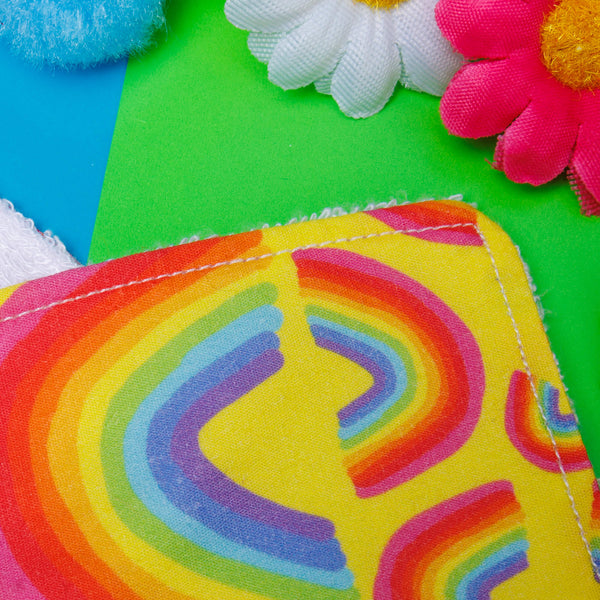 a bright yellow Reusable Makeup Remover Pad with rainbow illustrations by Katie Abey on it