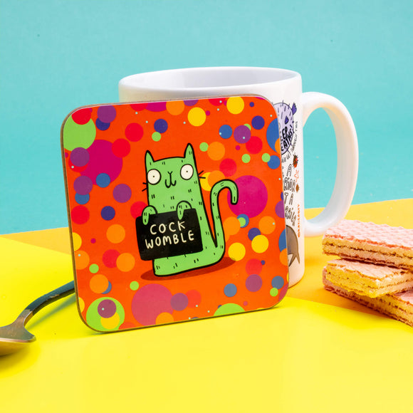 Sweary Womble Green Cat holding a sign saying, 'cock womble' on an orange background with multi coloured circles on a Coaster illustrated by Katie Abey