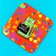 Sweary Womble Green Cat holding a sign saying, 'cock womble' on an orange background with multi coloured circles on a Coaster illustrated by Katie Abey