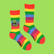 Katie Abey's vibrant rainbow socks with a green cat character and "Cock Womble" slogan. Featuring bold stripes and playful humour, these socks make an excellent gift or a statement piece for quirky fashion lovers. Support small businesses with this fun design.