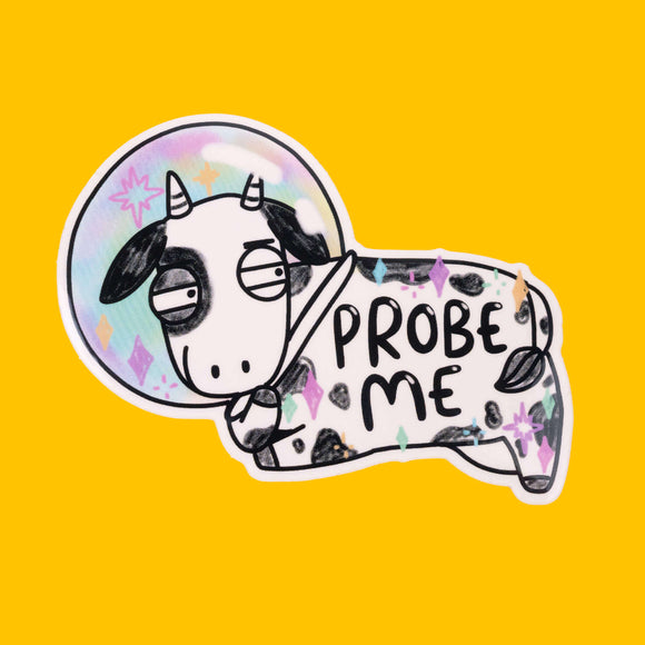 A sticker of a black and white cow in a rainbow-coloured space helmet, with the text "PROBE ME" on its body. The cow has a bored expression, and the background is bright yellow. This quirky design is from Katie Abey, a small colourful company for fun likeminded weirdos.