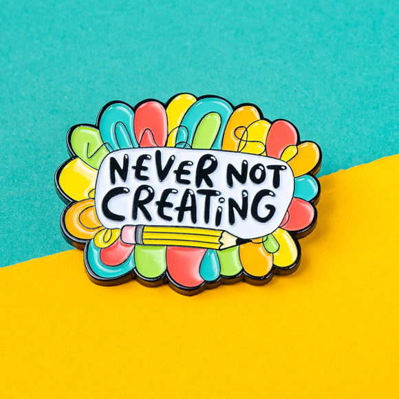 Close-up of the Katie Abey 'Never Not Creating' soft enamel pin. The pin showcases the motivational phrase in the centre, surrounded by vibrant colours and a pencil graphic. Ideal for anyone passionate about creativity and looking for a unique accessory.