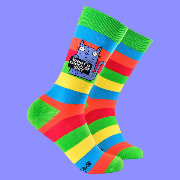 Bright rainbow-striped socks with green cuffs, heels, and toes, featuring Katie Abey's quirky illustration of a blue cat holding a sign that says, "What a crock of shit." A playful design from a small business encouraging you to embrace your weirdness.