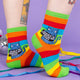 A model wearing Katie Abey socks with a blue cat holding a sign saying what a crock of shit. They are striped in rainbow colours and lovely and vibrant. The model is stood on a purple floor with purple with disco balls and ribbons