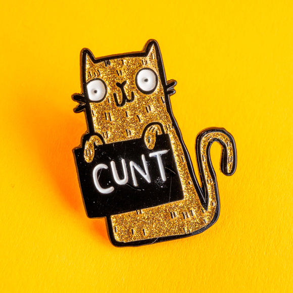 Close up of a gold glitter cat enamel pin with black outline and bold text on a sign, set against a vibrant yellow backdrop. This Katie Abey illustrated pin badge showcases a funny, irreverent design with a cute cat character, ideal for adding personality to jackets, bags or pin collections.
