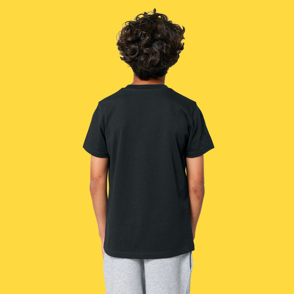 Back view of a child wearing the Cute But Feral Cat Kids T Shirt by Katie Abey in black. Short sleeve organic cotton tee with a relaxed unisex fit and plain back, photographed against a bright yellow studio background.