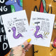 Two postcards next to each other featuring the empathic eel one they are empowered and the other 'not so great' the eel is purple and drawn by Katie Abey. It is shot with a white hand holding them against a shop window