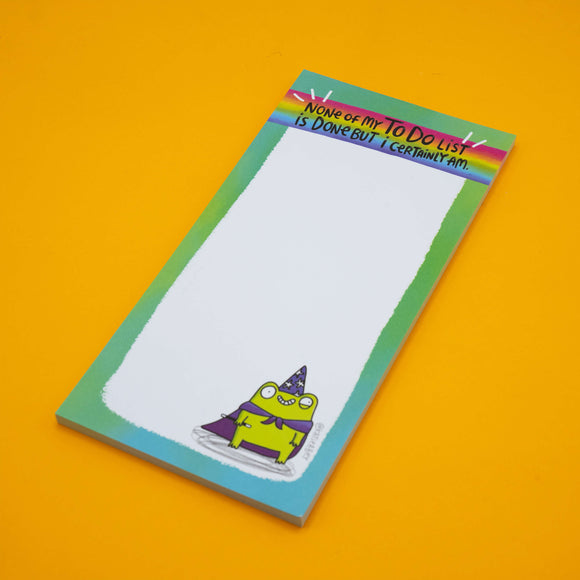 Katie Abey “None Of My To Do List Is Done But I Certainly Am” frog pad. Bright green frog wizard illustration with cape and hat sits at the bottom. Colourful rainbow header, perfect funny stationery for students and adults.