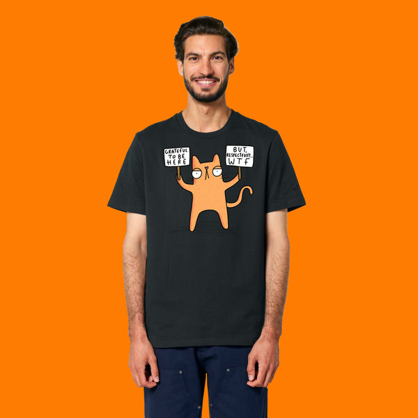 Front view of a model wearing the Katie Abey Grateful To Be Here But Respectfully WTF adults t shirt in black. The design features a quirky orange cartoon cat holding two signs reading “Grateful To Be Here” and “But Respectfully… WTF”. Humorous alternative graphic tee illustrated by Katie Abey.
