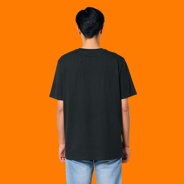 Back view of a model wearing the Katie Abey Grateful To Be Here But Respectfully WTF adults graphic t shirt in black. Unisex organic cotton tee with a relaxed fit and plain back, photographed on a bright orange background for an alternative fashion product listing.
