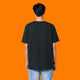 Back view of a model wearing the Katie Abey Grateful To Be Here But Respectfully WTF adults graphic t shirt in black. Unisex organic cotton tee with a relaxed fit and plain back, photographed on a bright orange background for an alternative fashion product listing.
