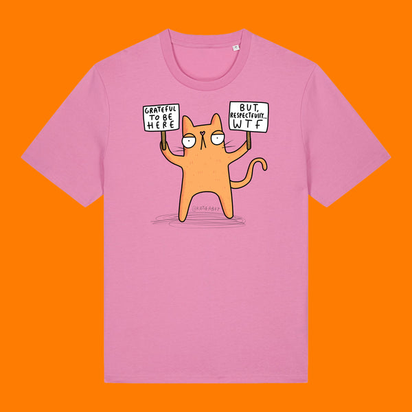 Front view of the Katie Abey Grateful To Be Here But Respectfully WTF bubble pink graphic t shirt. Features a quirky orange cartoon cat holding signs reading “Grateful To Be Here” and “But Respectfully… WTF”, illustrated by Katie Abey.