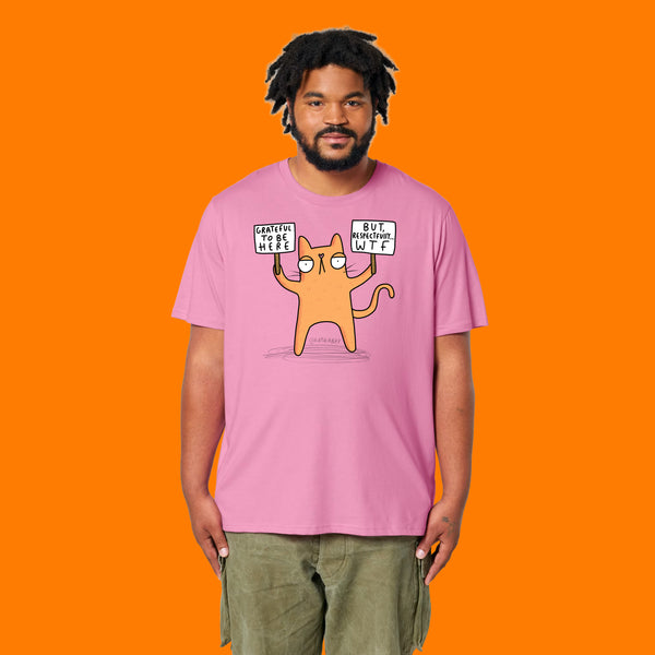 Front view of a model wearing the Katie Abey Grateful To Be Here But Respectfully WTF bubble pink adults t shirt. Funny alternative graphic tee featuring Katie Abey’s cartoon cat illustration holding humorous protest signs.
