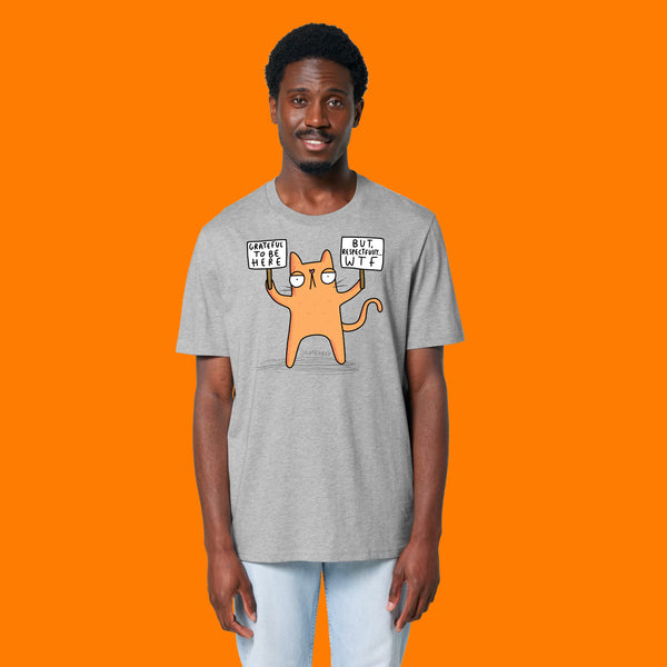 Front view of a model wearing the Katie Abey Grateful To Be Here But Respectfully WTF heather grey graphic t shirt. The design shows a cartoon cat holding protest signs with humorous wording. Quirky alternative fashion tee by illustrator Katie Abey.
