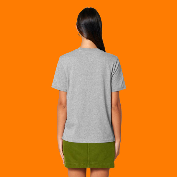 Back view of a model wearing the Katie Abey Grateful To Be Here But Respectfully WTF heather grey adults t shirt. Unisex fit organic cotton graphic tee with plain back, styled with a green skirt against an orange studio background.
