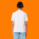Back view of a model wearing the Katie Abey Grateful To Be Here But Respectfully WTF adults t shirt in white. Unisex organic cotton tee with a classic fit and plain back, photographed against an orange background for an alternative fashion product listing.