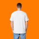 Back view of a model wearing the Katie Abey Grateful To Be Here But Respectfully WTF white graphic t shirt. Unisex organic cotton tee with relaxed fit and plain back, styled with light denim jeans against a bright orange studio background.