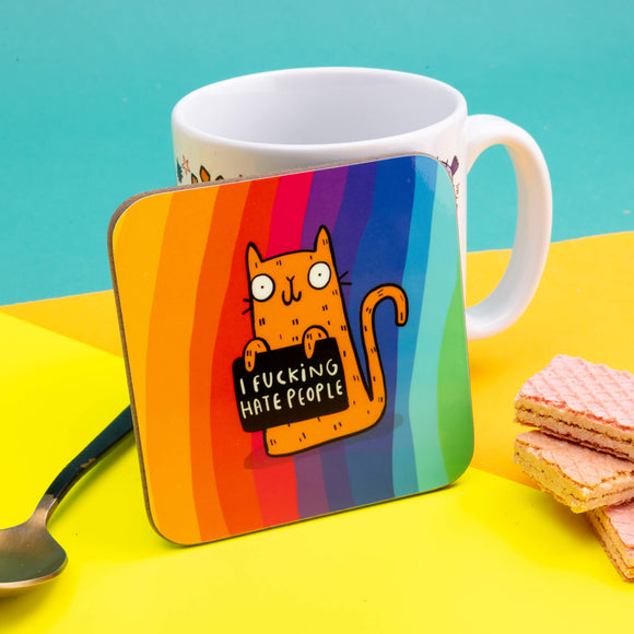 A coaster with a rainbow striped background with an orange cat on it illustrated by Katie Abey holding a sign saying 'I fucking hate people' on a colourful background.