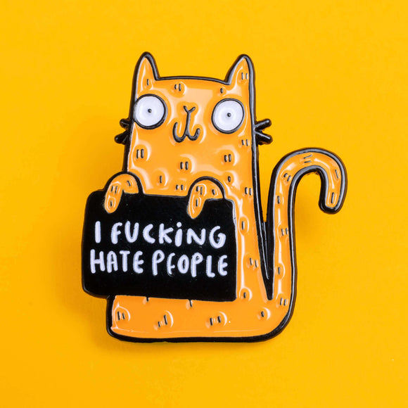 Katie Abey hand drawn illustration enamel pin featuring a bright orange cat with wide, bulging eyes and a mischievous expression, holding a black sign with the bold statement 'I Fucking Hate People'. The pin is on a bright yellow backdrop